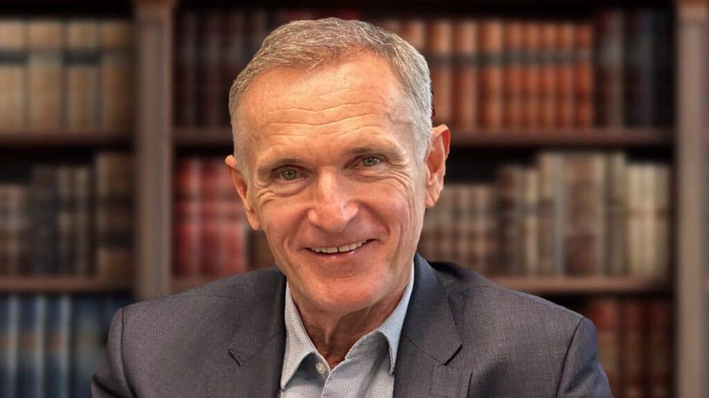 Egy középkorú férfi portréja könyvespolc előtt, elegáns öltözetben.