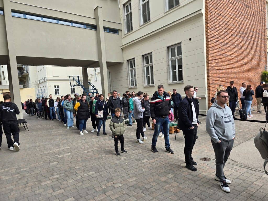 Emberek sorban állnak egy választási helyszínen, türelmesen várakoznak.