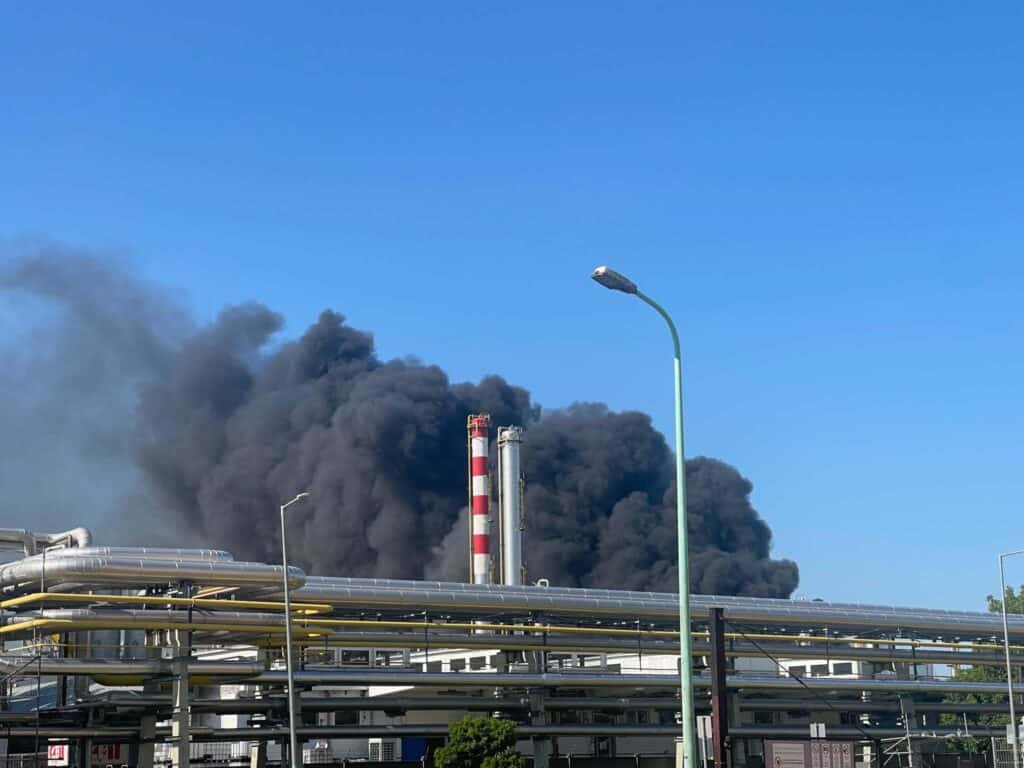 Fekete füst száll fel egy ipari létesítmény kéményéből, a tiszta kék ég ellenében.