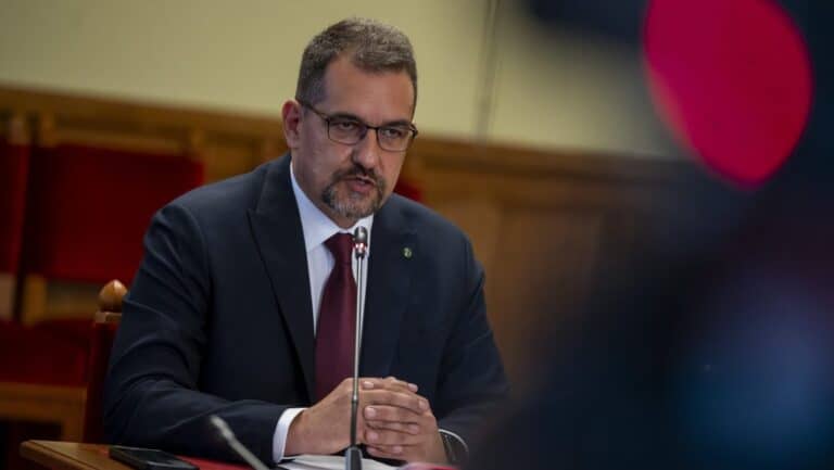 Ülésen ülő férfi, üzleti öltözet, szemüveg, komoly arckifejezés.