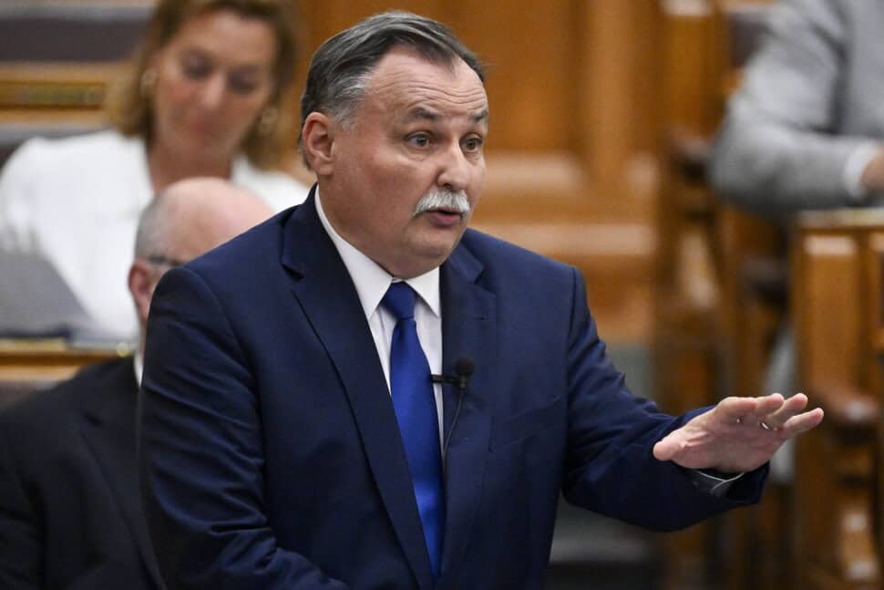 Magyar politikus beszél a parlamentben, kék öltönyben, komoly arckifejezéssel.