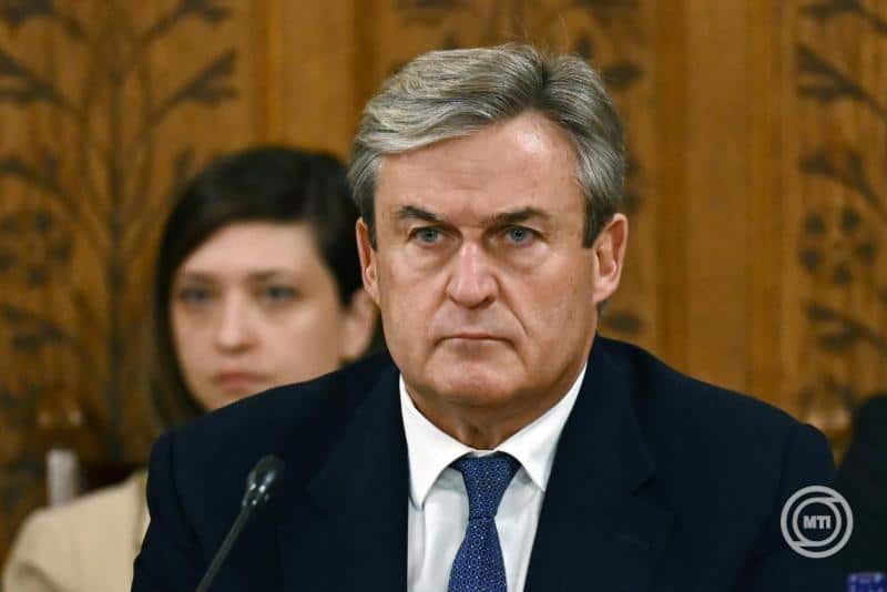 Magyar politikus ülésen, komoly arckifejezéssel, háttérben más személy.