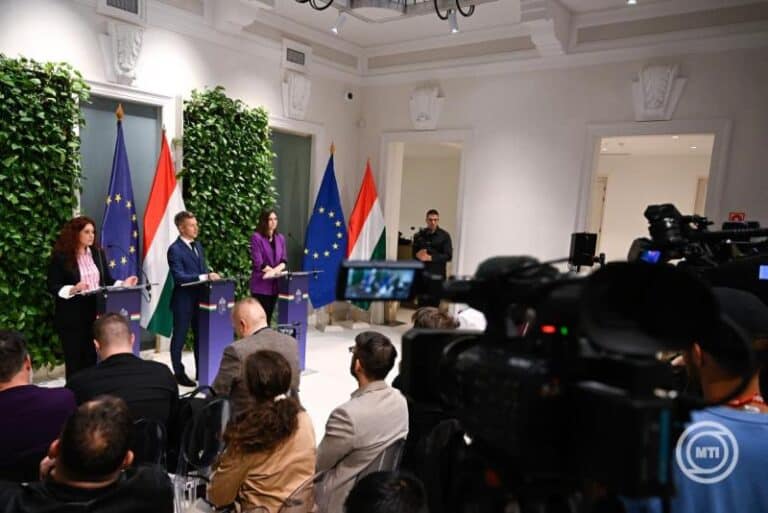 EU és magyar zászlók a háttérben, sajtótájékoztató a konferenciateremben.