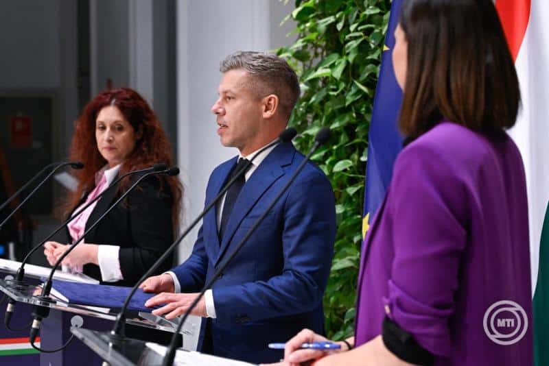Magyar politikusok sajtótájékoztatón, háttérben nemzeti és uniós zászlók.