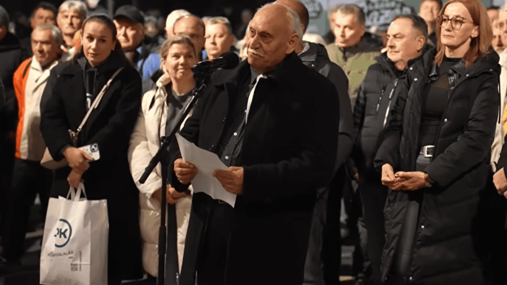 Csoport gyűlés, egy férfi beszédet mond, több ember hallgatja figyelmesen.