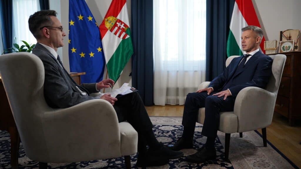EU és magyar zászlók a háttérben, két férfi beszélget az irodában.