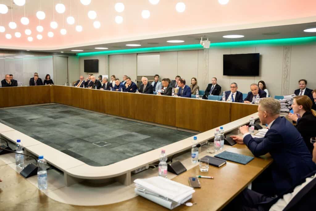 Politikai tárgyalás egy nagy tanácskozóteremben, sok résztvevővel.