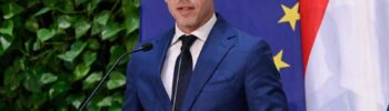 Magyar politikus beszédet mond az EU zászlók előtt.