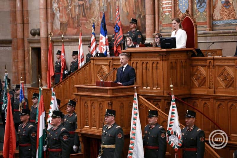 Magyar miniszterelnök beszédet mond a parlamentben, háttérben katonai díszszemle.