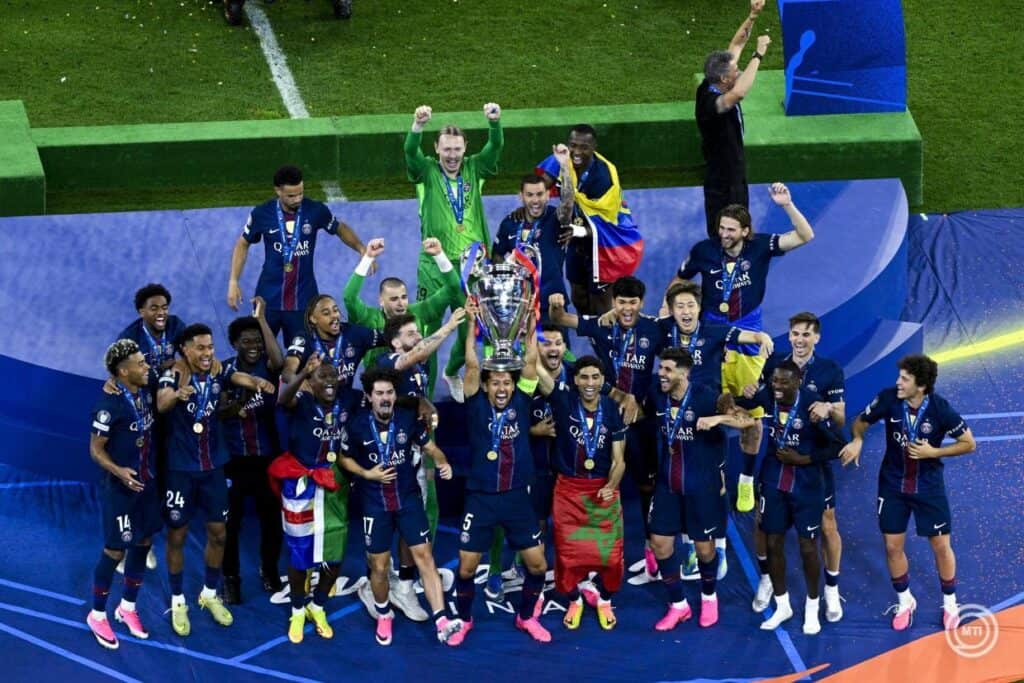 A PSG csapata ünnepli a bajnoki címet a pályán, a játékosok és a tréner is örömmel mutatják a trófeá.
