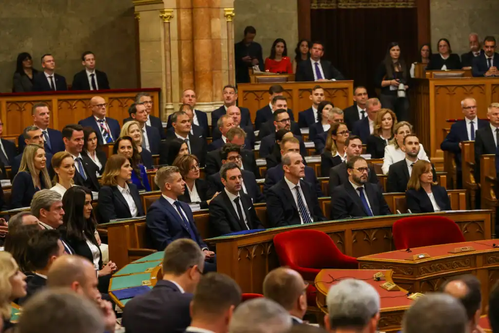 Politikai ülés a parlamentben, ahol képviselők és politikusok hallgatnak.