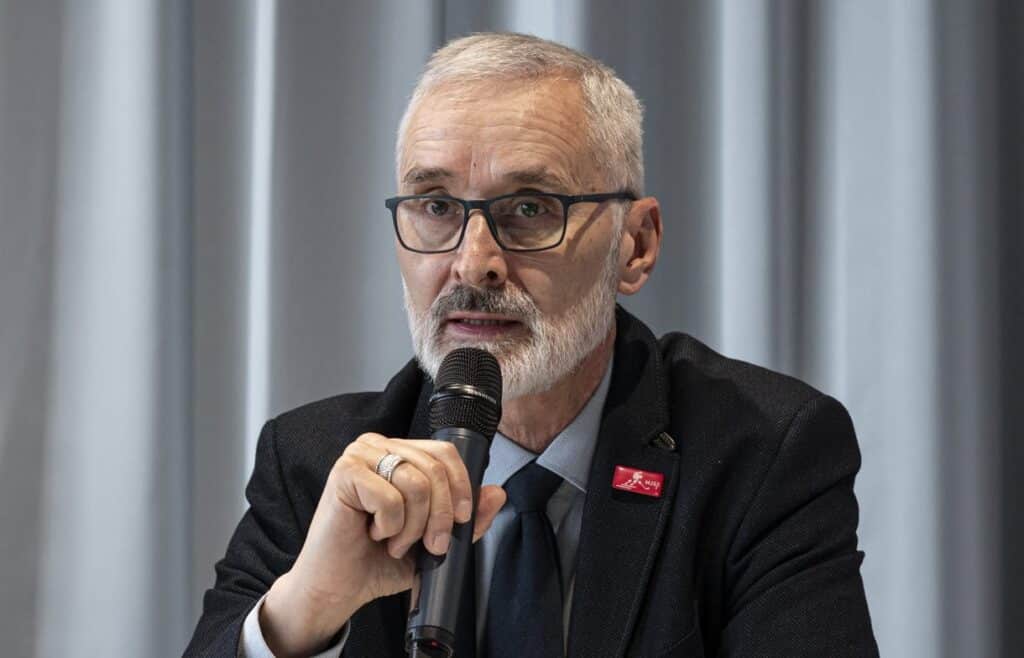 Férfi beszél egy mikrofonba, üzleti vagy konferencia környezetben.