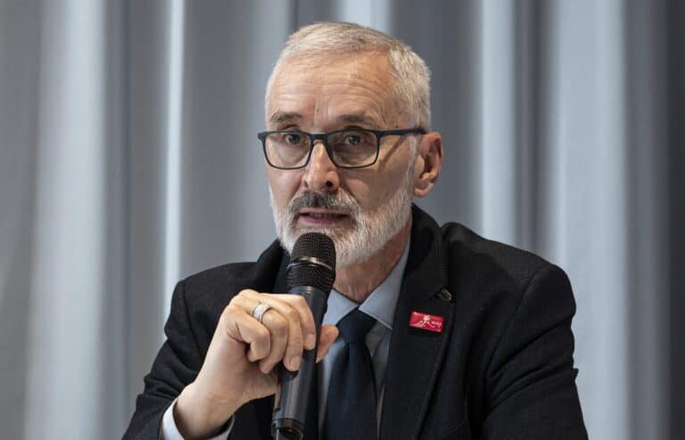 Férfi beszél egy mikrofonba, üzleti vagy konferencia környezetben.