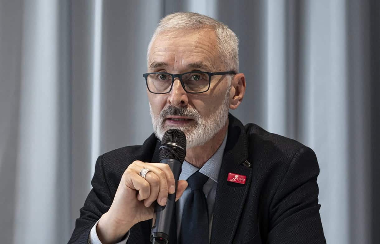 Férfi beszél egy mikrofonba, üzleti vagy konferencia környezetben.