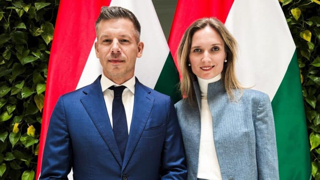 Magyar politikusok egy nemzetközi eseményen, magyar és uniós zászlók előtt.