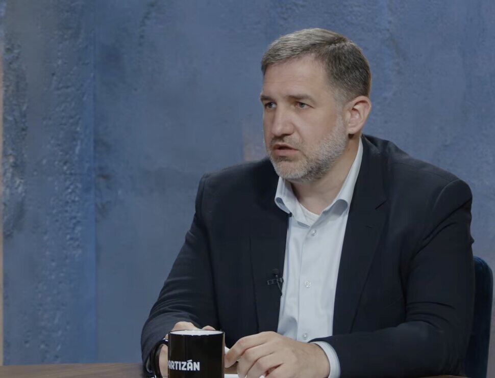 Magyar férfi beszélget egy műsorban, ül egy asztalnál, kávéval a kezében.