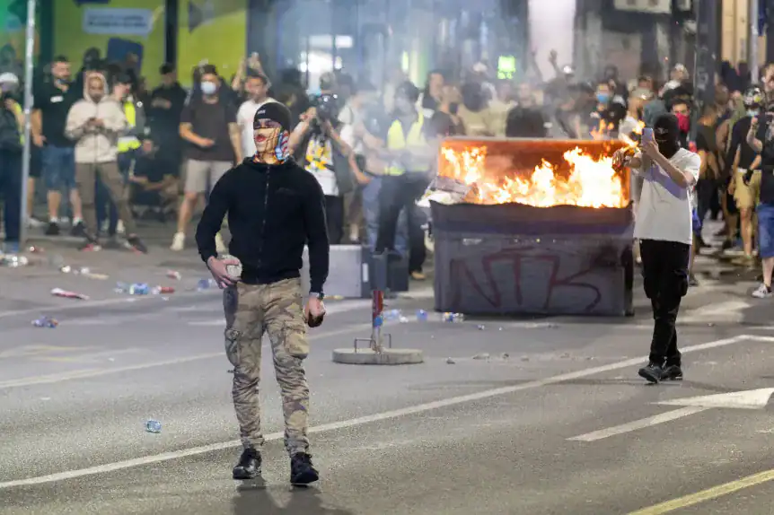 Fiatal férfi maszkban, tüntetés közben, lángoló konténer előtt Magyarországon.