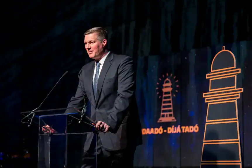 Magyar politikus beszédet mond egy konferencián, háttérben világító lámpás és feliratok.