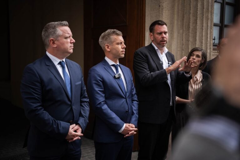 Politikai beszélgetés egy beltéri eseményen, három férfi és egy nő jelenlétében.