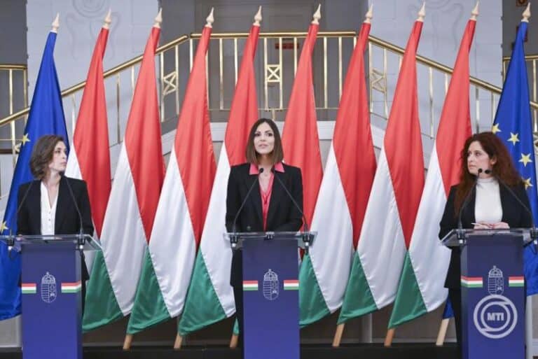 Magyar politikusok sajtótájékoztatón a nemzeti zászlók előtt.