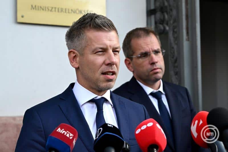 Két férfi politikus beszél sajtó előtt, mikrofonokkal körülvéve.