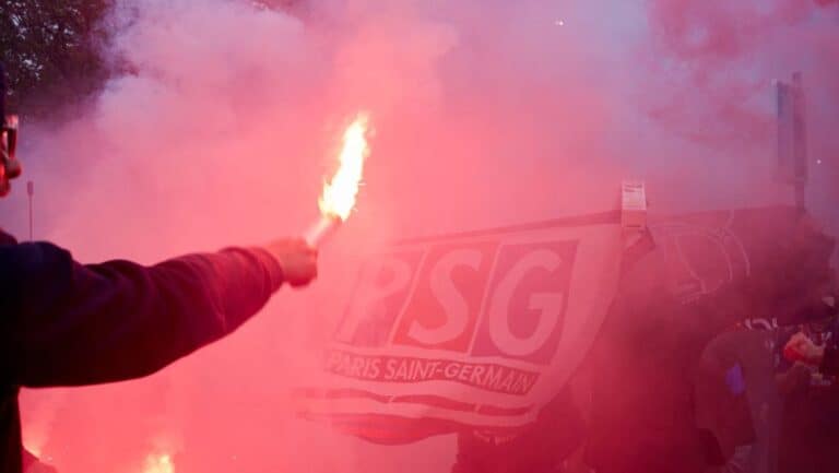 Foci füst és láng a PSG szurkolói szektorában, szurkolói zászló a háttérben.