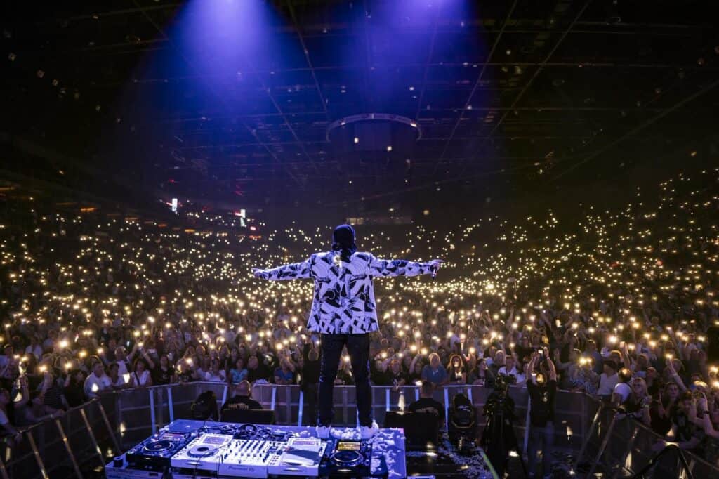Dj Dominique a színpadon, hatalmas közönség előtt, diszkófényekkel körülvéve.