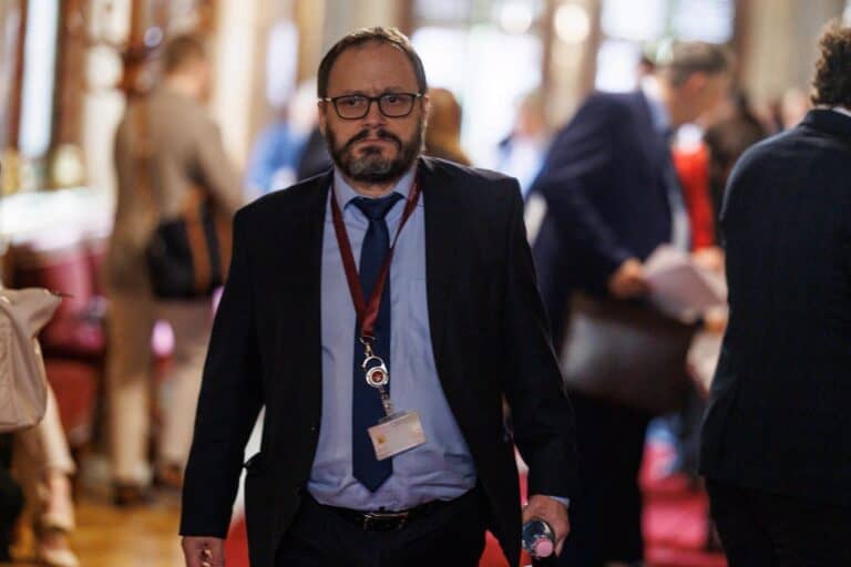 Férfi üzletember sétál egy konferencián, háttérben más résztvevők.