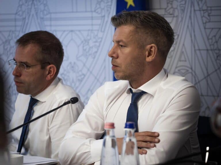 Politikai sajtótájékoztató két férfival, ülnek az asztalnál.