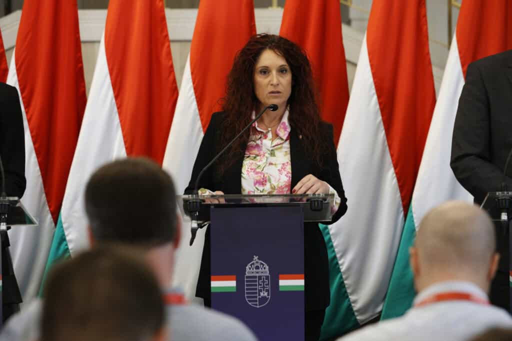 A magyar miniszter beszédet mond a nemzeti zászlók előtt.