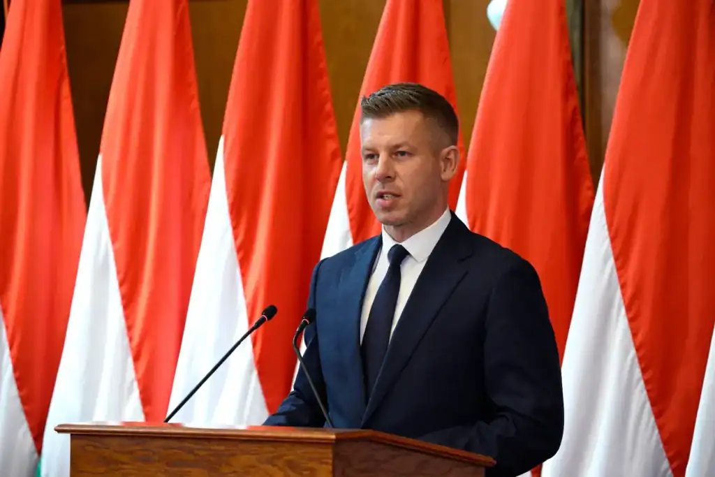 Magyar Péter beszédet mond a Sándor-palotában, háttérben magyar zászlók.