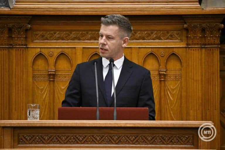 Főnök beszédet mond a parlamentben, háttérben díszes fafal.