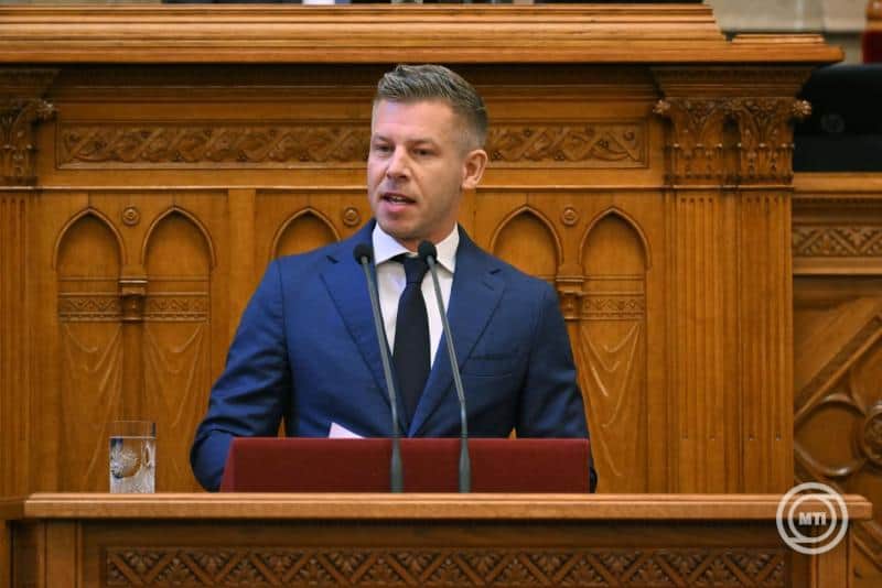 Magyar politikus beszédet mond a parlamentben, háttérben díszes fa fal.