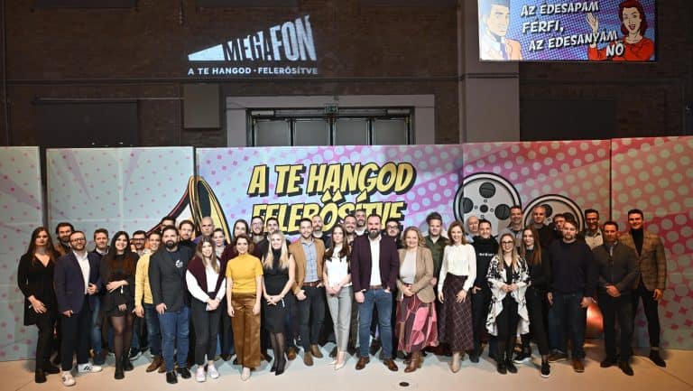 Sok ember csoportja egy színpadon, háttérben film és hangtechnika.