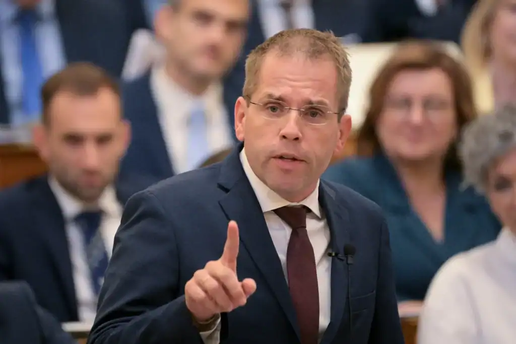 Politikus beszél egy konferencián, háttérben hallgatóság.