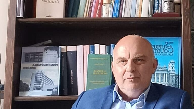 Férfi az irodában, könyvespolc előtt, üzleti ruhában.
