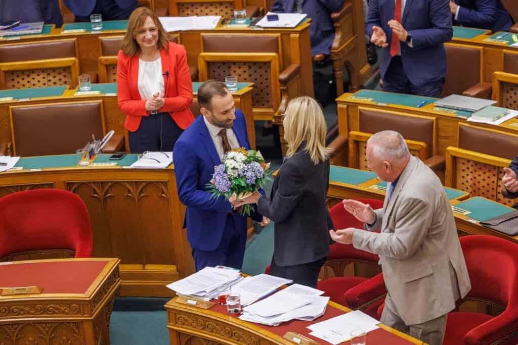 Görög Márta átadja a virágot egy képviselőnek a parlamentben.