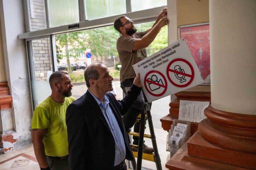 Hárman szerelik az arcfelismerő beléptető rendszert egy kórházi épületben.